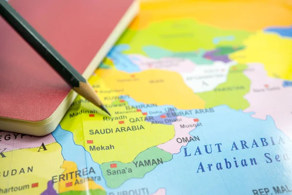 Saudi Arabia on a world map with book and pencil.