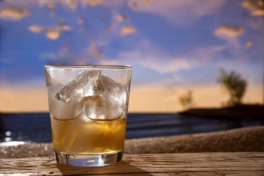 Kaya kokteylinin üzerinde viski, ahşap masa günbatımı plajı arka planında içki.