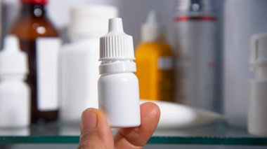 hand hold eye drops bottle in front of medicine cabinet