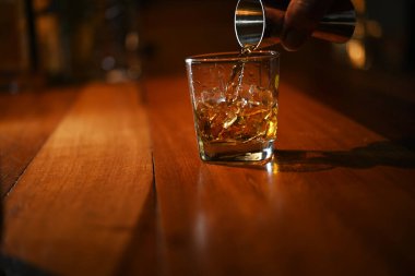 Bardaki buz bardağına viski dökerek.