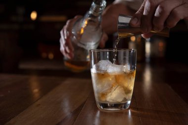 man hands pouring whisky from jigger into glass