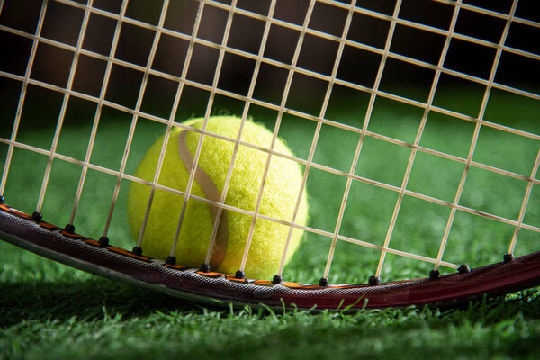 a portion of tennis racket with ball on grass court
