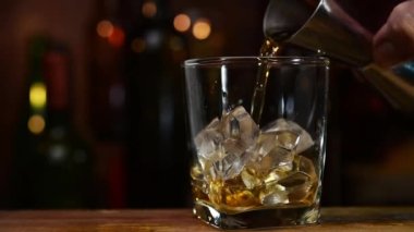 Viski jigger 'dan buz bardağına dökülüyor, viski kayanın üstünde.