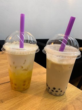 Şeffaf tek kullanımlık plastik bardakta kubbe kapaklı köpüklü süt çayı. Mor jumbo plastik pipetli buzlu (veya boba) sütlü çay içeriyordu..