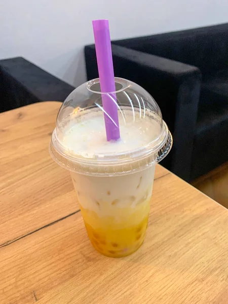 Bubble milk tea in the transparent disposable plastic glass with a dome lid. It contained iced bubble (or boba) milk tea with a violet jumbo plastic drinking straw.