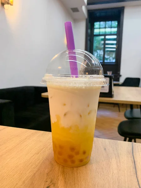 Bubble milk tea in the transparent disposable plastic glass with a dome lid. It contained iced bubble (or boba) milk tea with a violet jumbo plastic drinking straw.