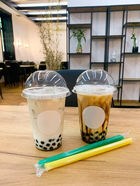 Şeffaf tek kullanımlık plastik bardakta kubbe kapaklı köpüklü süt çayı. Yeşil ve sarı jumbo plastik pipetli buzlu (veya boba) sütlü çay içeriyordu.