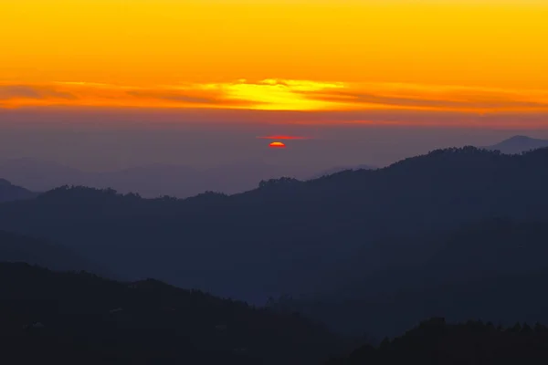 last light of sunset on the sky and orange cloud rays around the sun over the Mountains of Uttarakhand