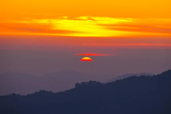 last light of sunset on the sky and orange cloud rays around the sun over the Mountains of Uttarakhand