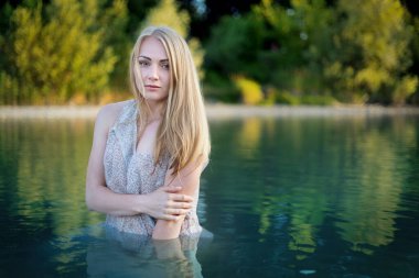 Uzun gecelikli sarışın kız gölde banyo yapıyor.