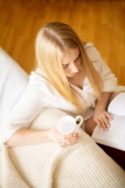 Kadın sabahları evde gömleğiyle kitap okuyor. Evde kitap okuyarak rahatlıyorum. Sabah kahvesi.