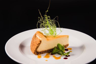 Siyah arka planda yuvarlak beyaz bir tabakta süslemeli peynirli pasta.