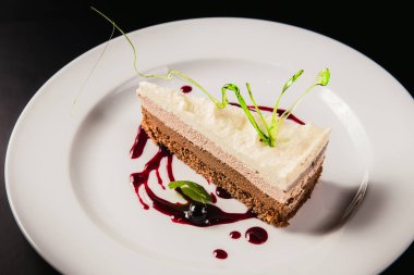 Siyah arka planda yuvarlak beyaz bir tabakta süslemeli katmanlı kahve keki.