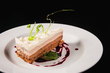 Siyah arka planda yuvarlak beyaz bir tabakta süslemeli katmanlı kahve keki.