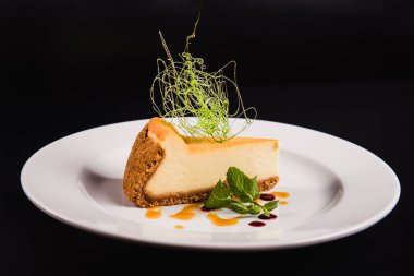 Siyah arka planda yuvarlak beyaz bir tabakta süslemeli peynirli pasta.