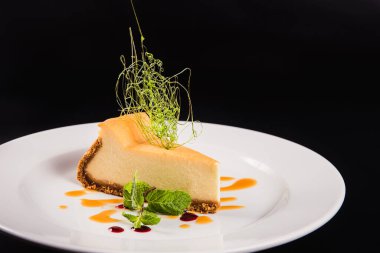 Siyah arka planda yuvarlak beyaz bir tabakta süslemeli peynirli pasta.