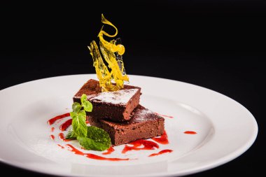 Siyah arka planda yuvarlak beyaz bir tabakta süslemeli katmanlı kahve keki.