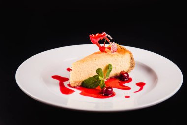 Siyah arka planda yuvarlak beyaz bir tabakta süslemeli meyveli pasta.