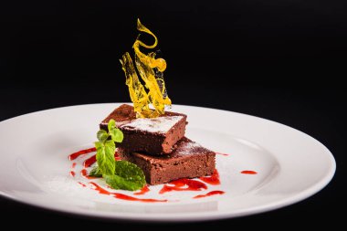 Siyah arka planda yuvarlak beyaz bir tabakta süslemeli katmanlı kahve keki.