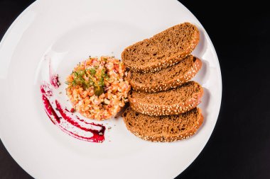 Somonlu salata ve siyah arka planda beyaz tabakta kahverengi ekmek. Tarta