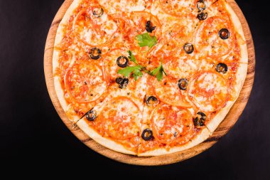 Siyah arka planda tahta bir tahtada zeytinli ve domatesli pizza.