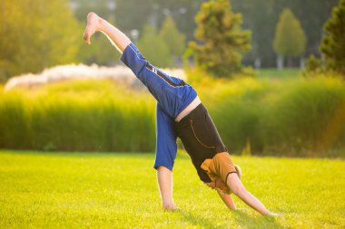 Çok esnek bir genç adam gün batımında çimlerde yoga yapıyor.