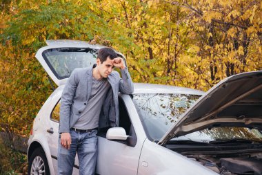 Bir adam açık kaputun altına bakar. Araba yolda bozuldu..