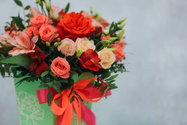 Kırmızı gül buketi, alstromerya ve gri arka planda yeşil bir kağıt hediye kutusunda östoma..