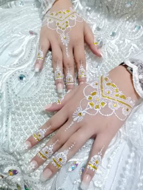 Gelinin elinde dantelli, kolyesi ve incili beyaz bir gelinlik var..