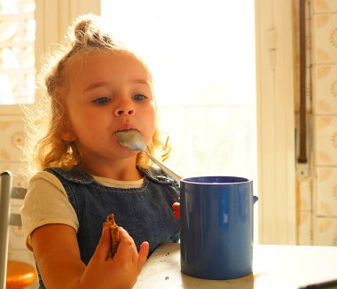 Küçük kız evde kahvaltı yapıyor okula gitmeye hazırlanıyor.