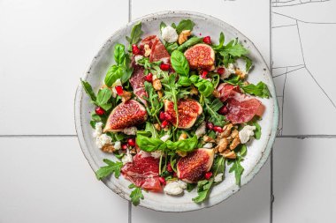 İncirli salata, prosciutto, roka, keçi peyniri, fındık ve nar tohumlu beyaz fayanslı. Üst Manzara. Sağlıklı diyet yemekleri