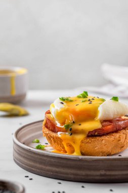 Benedict usulü yumurta. Haşlanmış yumurta, jambon, holandez sosu, lezzetli kahvaltı için dilimlenmiş tost üzerine soğan. dikey yönelim. İngiliz brançı