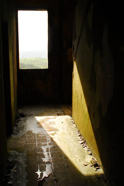 Sunlight through an open window leaves shadows in dark hallway of old, empty, abandoned building in Asia.