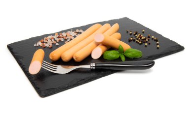 Kaynamış tavuk sosisleri siyah taşlı servis tahtasında, beyaz arka planda izole edilmiş..