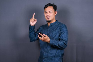 Gri arka planda izole edilmiş genç Asyalı bir adam bir ürün sunmak için kenarı işaret ediyor.