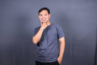 Bazı şeyleri düşünen Asyalı genç bir adam, gri arka planda izole edilmiş. Model kopyalama alanı