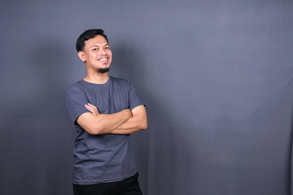Smiling handsome man in gray t-shirt standing with crossed arms isolated on gray background