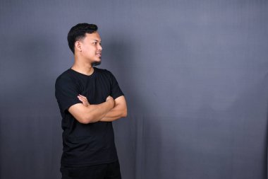 Siyah tişörtlü gülümseyen Asyalı adam gri arka planda kollarını kavuşturmuş duruyor.