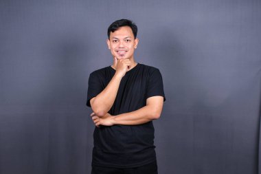 Asyalı genç adam siyah tişört giyip bir şeyler düşünüyor. İzole edilmiş gri arkaplan