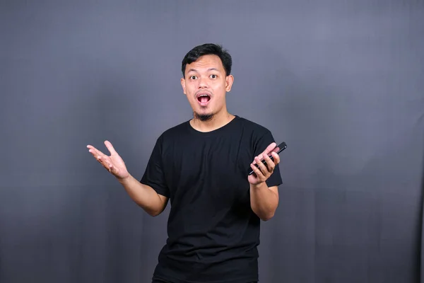 Amazed excited young asian man looking at camera with wow face expression feeling surprised advertising shopping promotion, unbelievable win standing isolated on gray background.