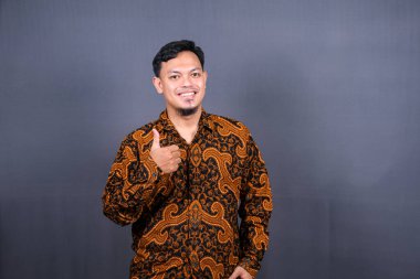 Gri arka planda izole edilmiş Batik pozlar veren Asyalı bir gencin portresi.