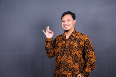 Yüzük hareketini parmaklarıyla gösteren çekici bir Asyalı. Yakın plan portre, iyi iş, uzlaşma konsepti. Ben iyiyim, onaylıyorum. Adam öneriyle tatmin oluyor. Gri arkaplanda izole