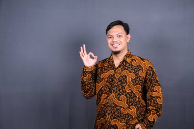 Yüzük hareketini parmaklarıyla gösteren çekici bir Asyalı. Yakın plan portre, iyi iş, uzlaşma konsepti. Ben iyiyim, onaylıyorum. Adam öneriyle tatmin oluyor. Gri arkaplanda izole