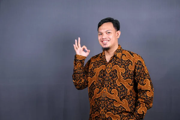 Gri arka planda izole edilmiş Batik pozlar veren Asyalı bir gencin portresi.