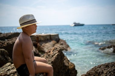 Şapkalı bir çocuk deniz kenarındaki bir kayanın üzerinde oturuyor. Profil fotoğrafı