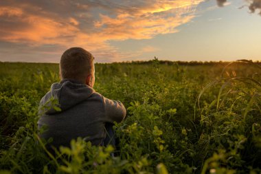 Bir çocuk yonca tarlasında oturur ve gün batımını izler. Çocuğun dikiz aynasından. Gün batımının güzel renkleri gökyüzünde güneş yüzünde parlarken. kırsal cennet