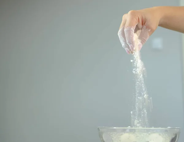 Kurabiye. Elden bir kaseye un dökülüyor. Un parçacıkları el ele uçar. Bir kızın elinin bir kaseye un dökerken çekilmiş yakın plan fotoğrafı. görünür un parçacıkları