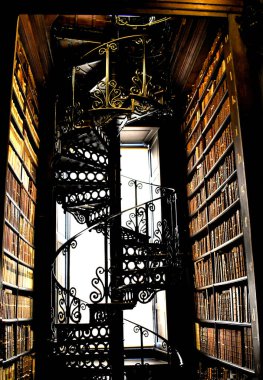 Aydınlatılmış pencerenin önünde bir sürü eski kitapla eski bir kütüphanenin ortasındaki sarmal merdiven.