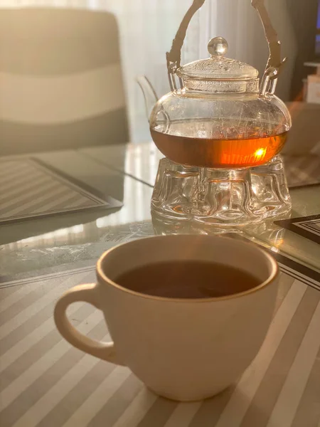 Beyaz bardakta çay, cam çaydanlığın yanında.