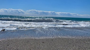 Dalgalar, beyaz köpük ve çakıl plajı.